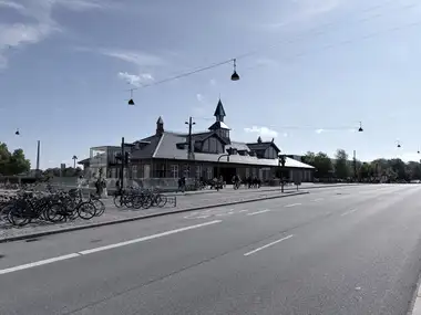 A wide view across Oslo Plads shows the long street facade, twin lunette gables, slate roof and central clock tower with spire.