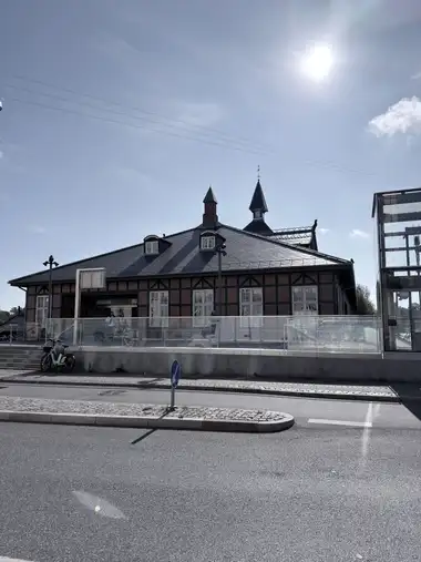 The low street facade of Østerport Station is seen across the road, with brick-and-timber walling, a broad slate roof, dormers, rooftop towers and part of the modern glass entrance structure.