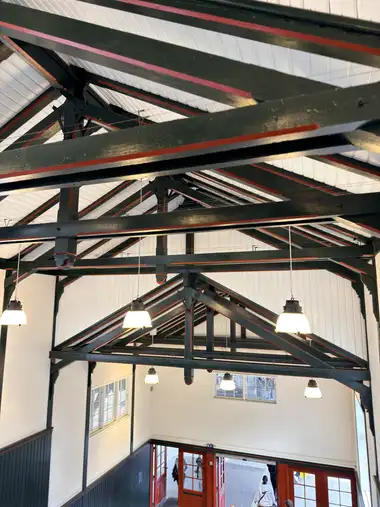 Painted green-and-red roof trusses, white boarded roof slopes and suspended pendant lights span the station entrance hall above red glazed doors.