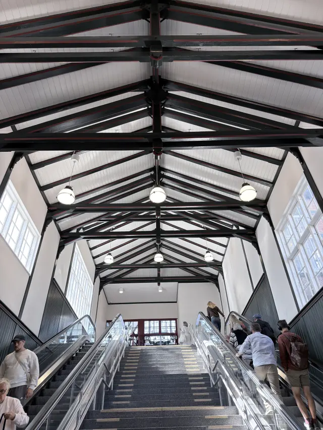 Open timber trusses painted green and red over a stair hall leading down to the platforms.