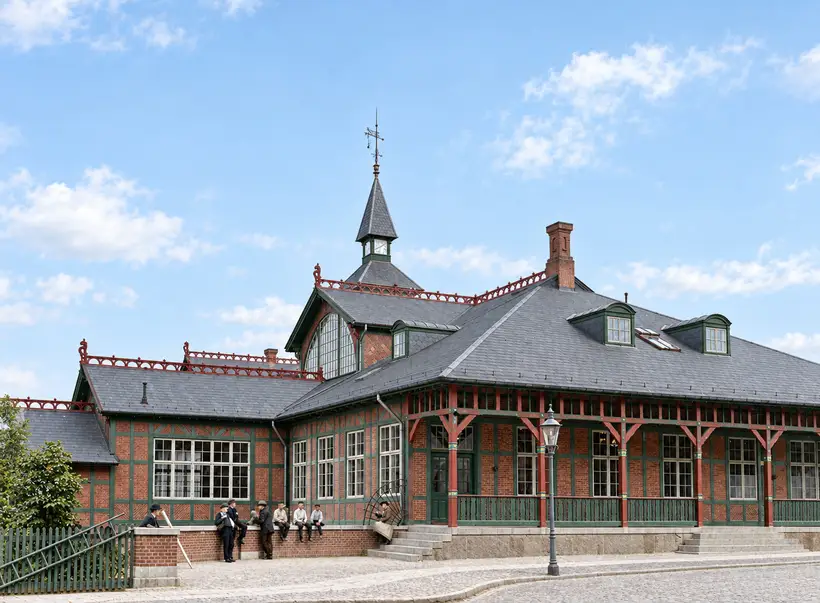 Østerport Station with steep roofs, a central tower, covered veranda and people gathered beside the entrance.