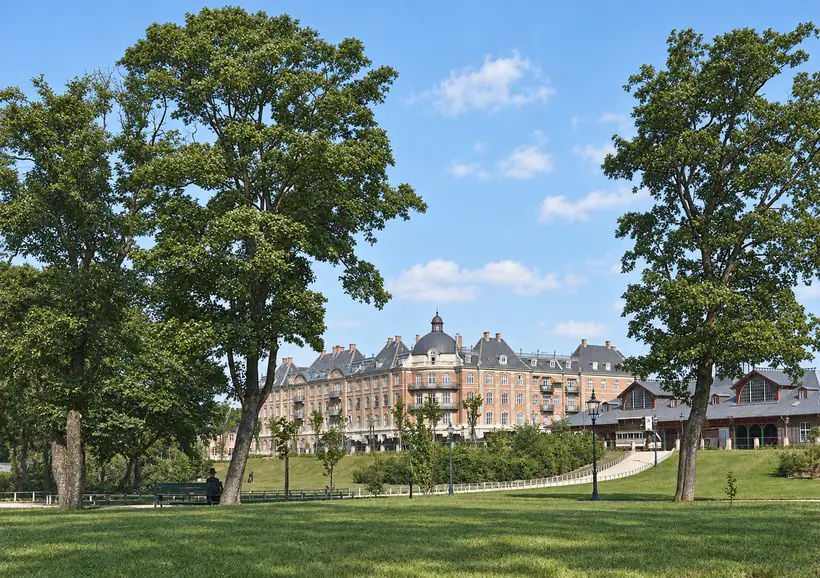 Park lawns and mature trees frame Østbanegården beside a large residential building, with paths, benches and several people.