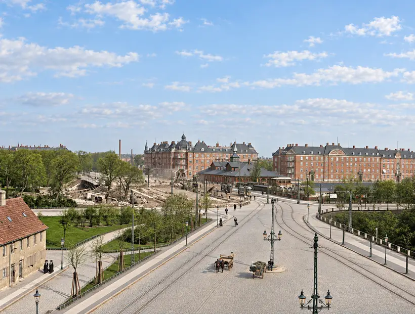 Elevated view along Grønningen toward Østbanegården, with tram tracks, horse-drawn vehicles, pedestrians, trees and apartment buildings.