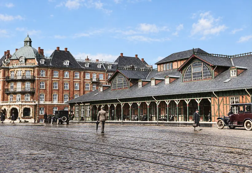Østerport Station faces a cobbled forecourt with tram rails, pedestrians and motor cars, while a large residential building rises behind.