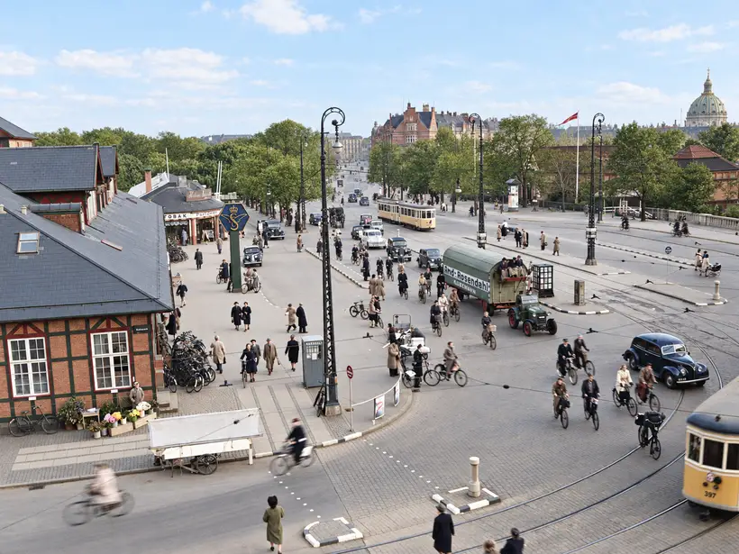 Elevated view across Østbanegården, a tram-lined intersection crowded with cyclists, pedestrians, cars and a delivery truck.