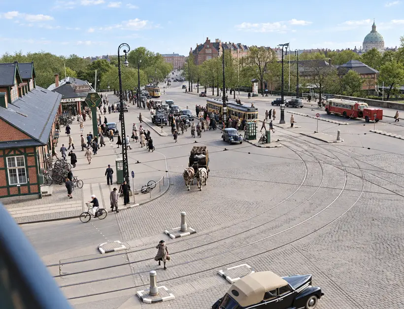 Elevated view outside Østbanegården with station buildings, tram tracks, trams, buses, cars, cyclists, pedestrians and a horse-drawn cart.