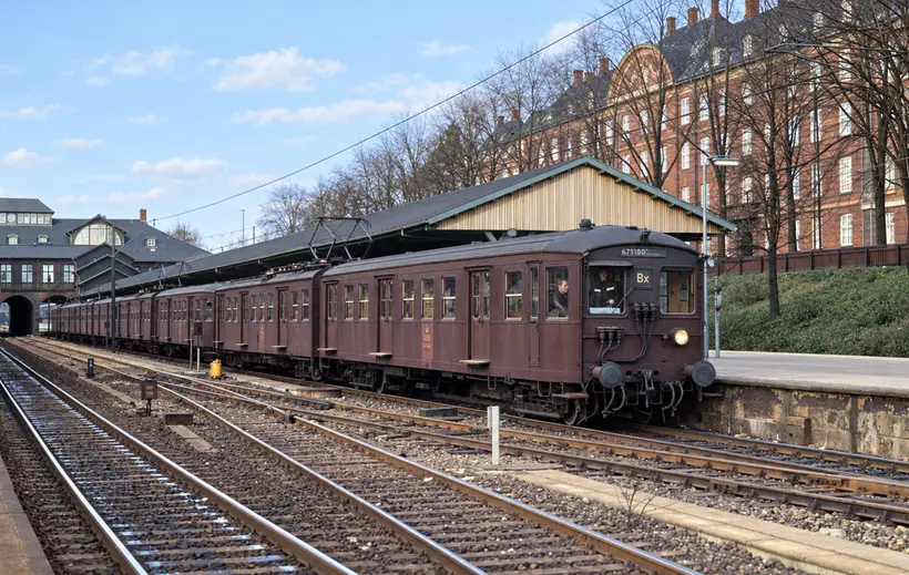 An electric train stands beside a covered platform at Østerport Station, with railway tracks, station buildings and passengers visible.