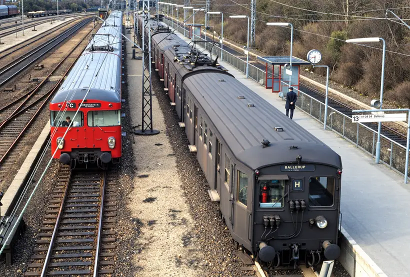 Two electric trains stand beside platforms and tracks beneath overhead wires at København Østerport Station.