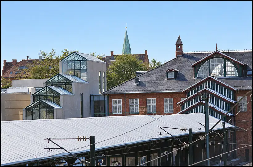 A stepped glazed stair enclosure rises beside Østerport Station, above platform roofs and overhead railway wires.
