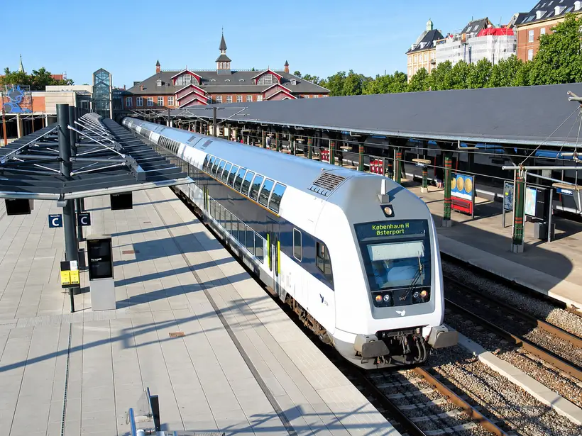 A double-decker train stands beside covered platforms, with Østerport Station’s main building visible beyond the tracks.