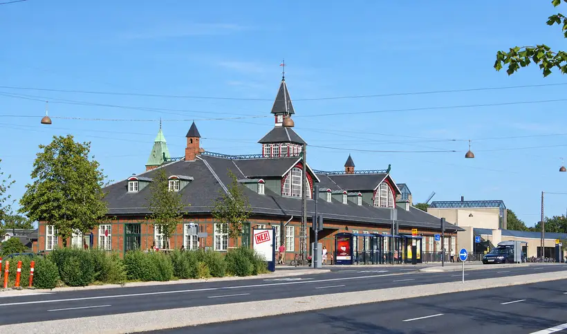 København Østerport Station viewed across Oslo Plads, with steep roofs, towers, an entrance canopy, street traffic, and overhead transit wires.