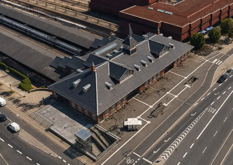 The station building seen obliquely from above, with slate roofs, a tower, platforms, trains and broad city streets around the complex.