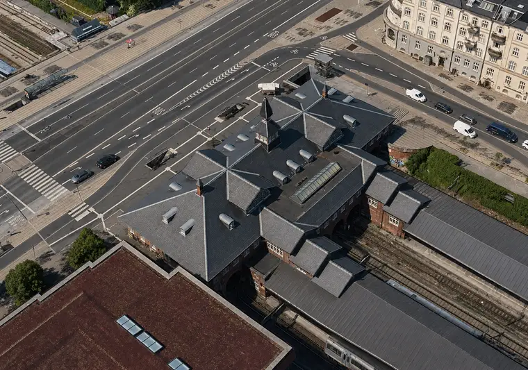 The station building seen from high above with slate roofs, towers, skylights, platforms, railway tracks and a large road junction around it.
