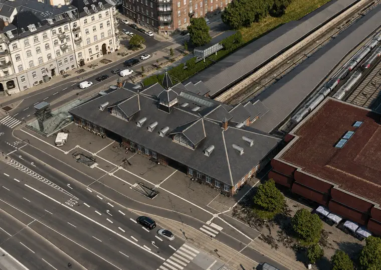 The station building is seen obliquely from above between a broad city street, railway platforms, tracks and dense residential blocks.