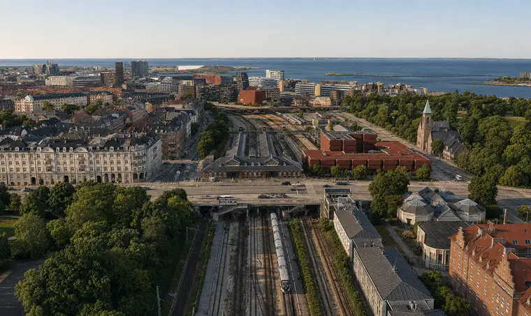 The long station building spans the railway corridor between dense city blocks, green parks and the waterfront.