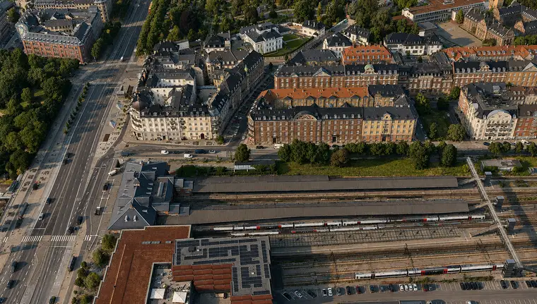 The railway station with station buildings, covered platforms and tracks between a broad boulevard and dense residential blocks.