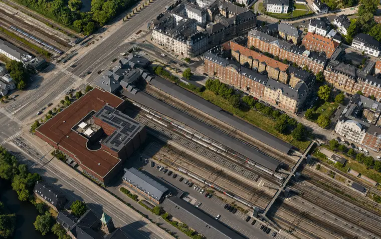 The station complex with platform roofs, trains and tracks lies between a broad city street and dense residential blocks.