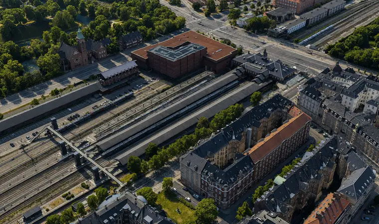 The station building and covered platforms sit among railway tracks, a church, green spaces and dense residential blocks.