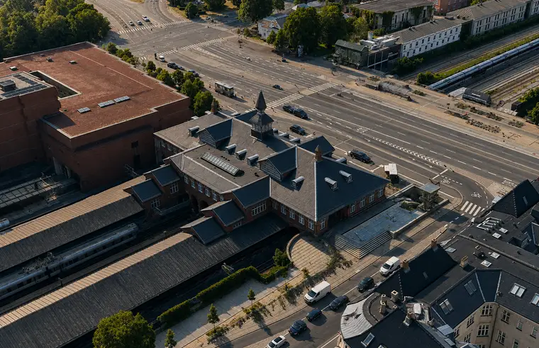 The station building with its tower, slate roofs and platforms stands between railway tracks, broad roads and dense urban blocks.