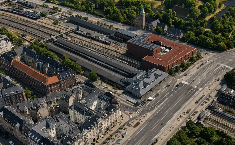 The red-brick station building stands among tracks and platforms, surrounded by apartment blocks, broad roads and a wooded park.