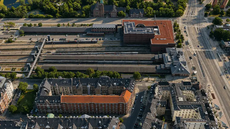 The station building and long platform roofs sit between railway tracks, apartment blocks and a broad city avenue.