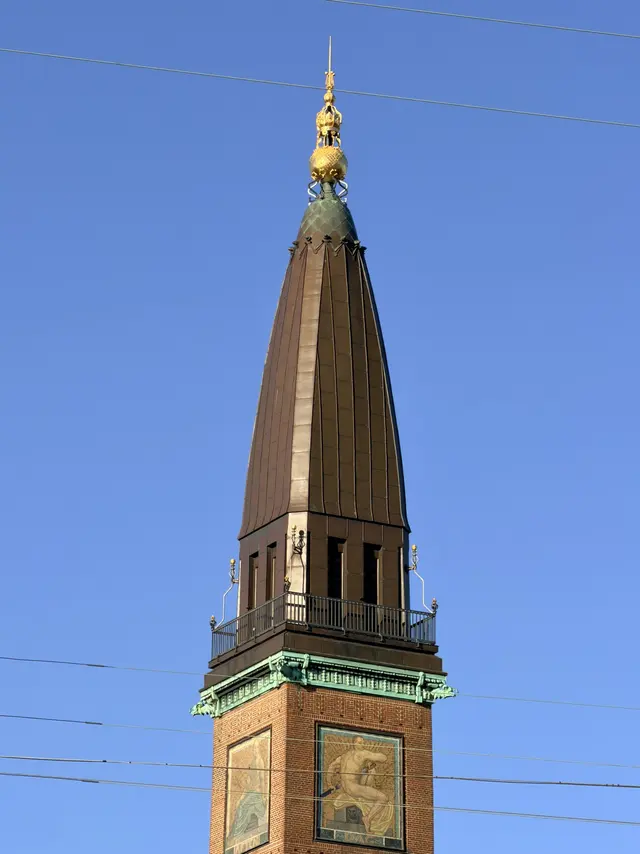 Tårnets kobberbeklædte spir mod en klar himmel, med forgyldt kugle og spir øverst.