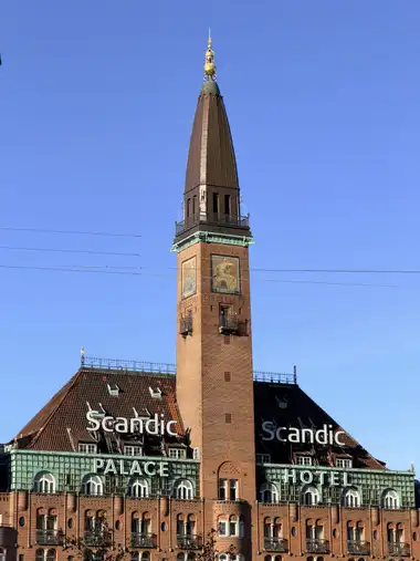 Oversigtsbillede af palace hotel midterste tårn set fra pladsen, i tegl, fliser, kobber og metal.