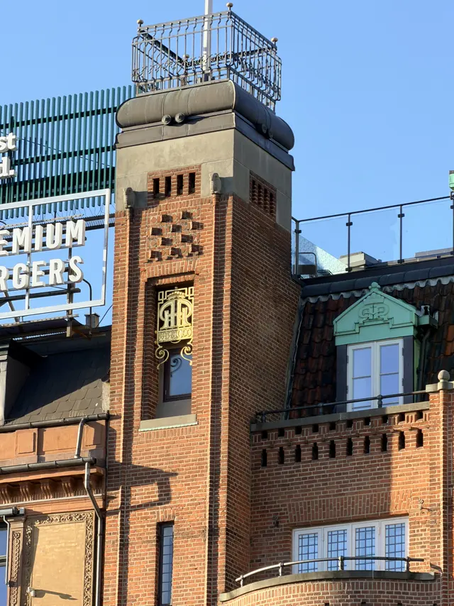 Et forgyldt felt på flagtårnets skaft: en krone over et sammenslynget monogram, og under det en strimmel med teksten AAR 1909.