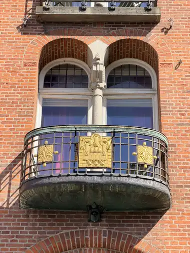 Billede af forgyldt altan rækværk på gadefacaden, i tegl, mørtel, granit og træ.