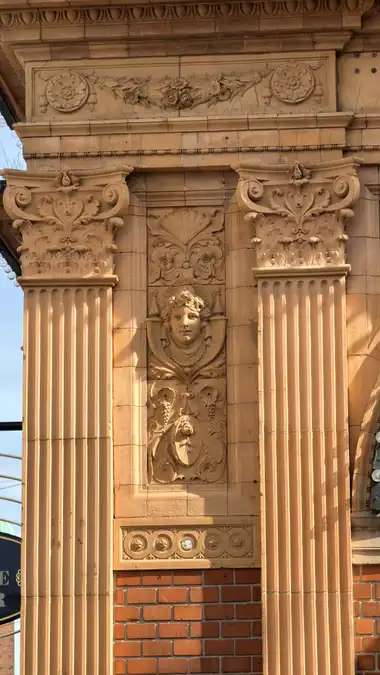 Nærbillede af kvindelig ansigt pilaster relief ved sidebygningen, i tegl, mørtel og metal.