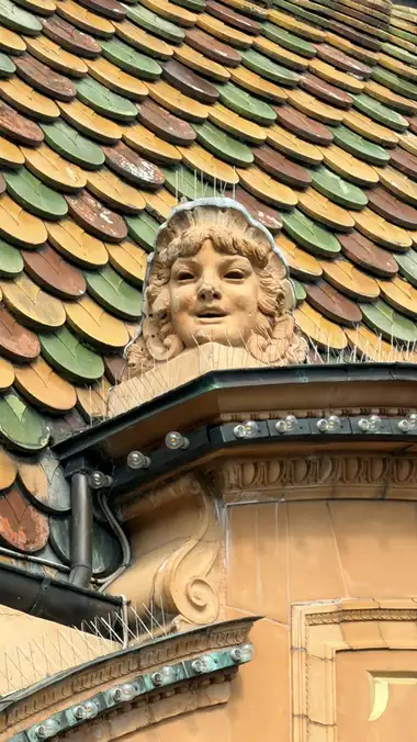 Nærbillede af smilende menneske ansigt maske langs facaden, i glas, kobber, metal og stål.