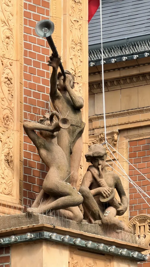Tre børn i ler til højre for buen blæser i en lang trompet, et buet horn og en fløjte.