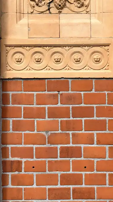 Nærbillede af terrakotta roset frise ved sidebygningen, i tegl og mørtel.