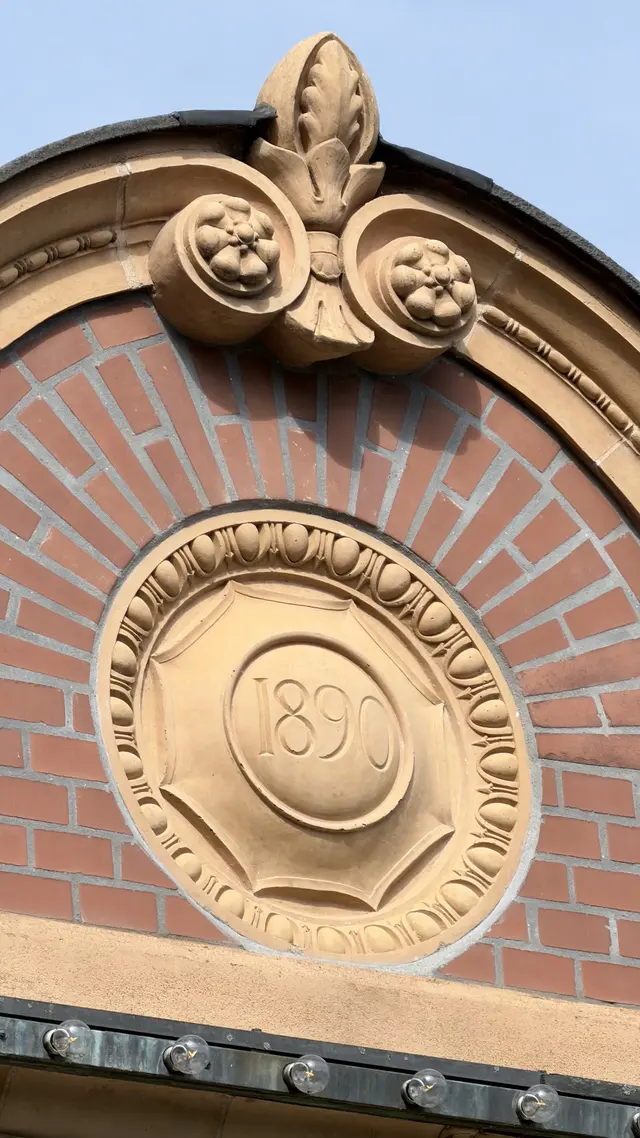 En rund sten med årstallet 1890 i en vifte af røde mursten, indrammet af en æg-og-pil-bort og en bladspids.