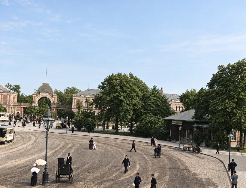 Set fra et vindue højt over Axeltorv: porten og pavillonerne på den anden side af den åbne plads, med sporvogne, vogne og en kvinde med parasol i forgrunden.