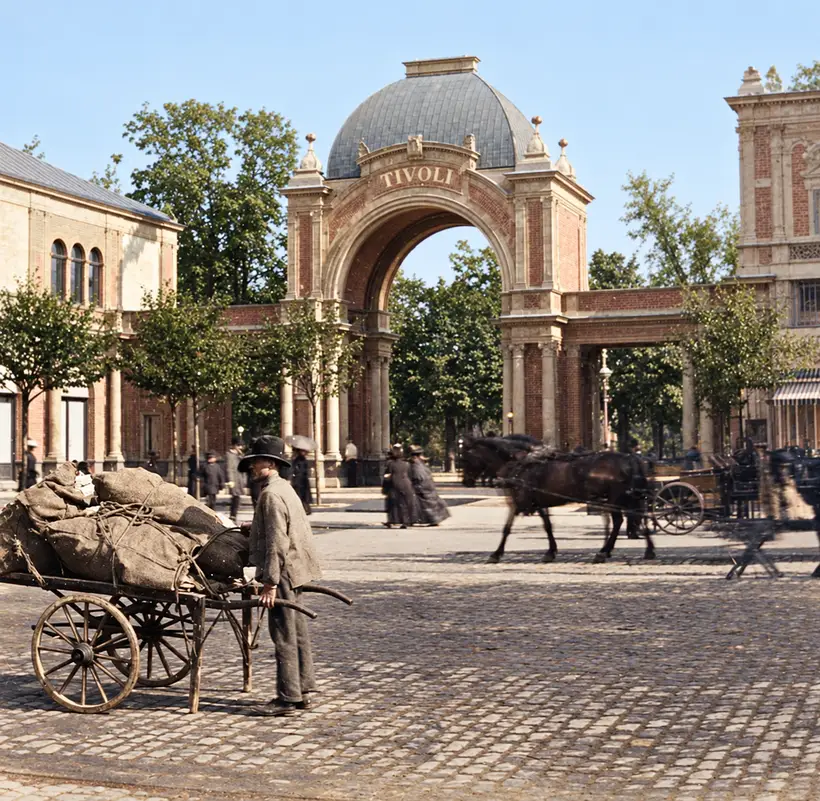 Porten fra 1890 set fra Vesterbrogade: kuplen, TIVOLI på buen, de lave arkader og en pavillon til højre; foran en mand med en trækvogn læsset med sække, hestevogne bagved.