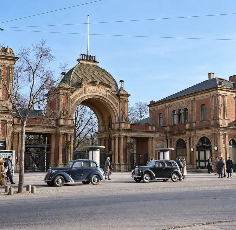 Porten set lige forfra fra Vesterbrogade: biler fra 1950’erne ved kantstenen, plakatsøjler, fodgængere, nøgne træer og en pavillon på hver side.
